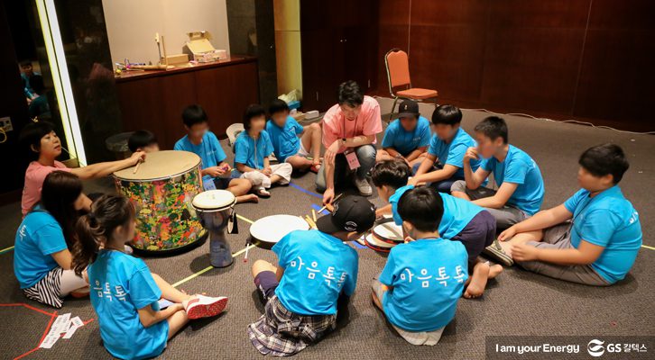 아이들이 바닥에 둘러앉아 치료사 선생님의 북소리를 들으며 노래로 속마음을 이야기하고 있다.